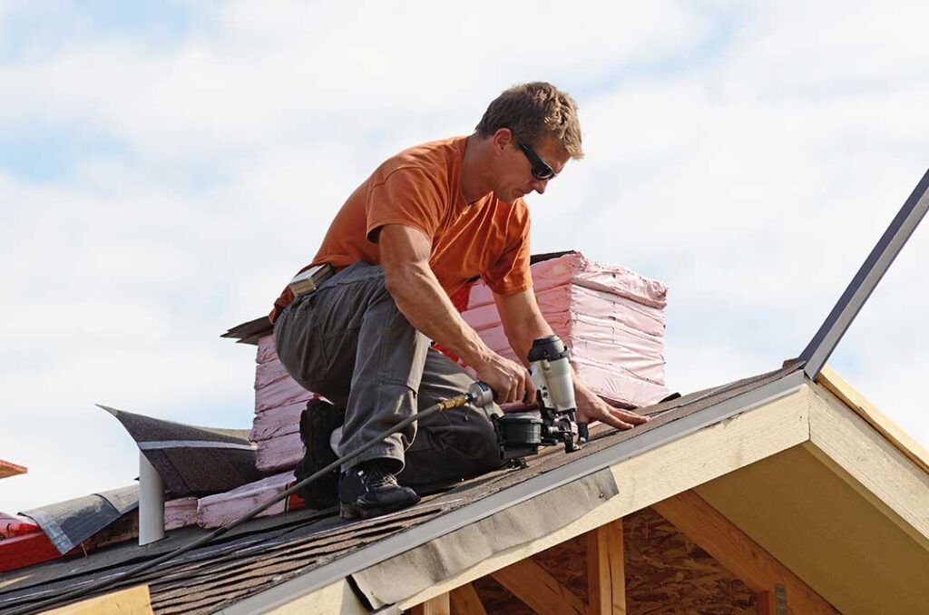 Building official inspecting roof sheathing and ice barrier on a winter home.
